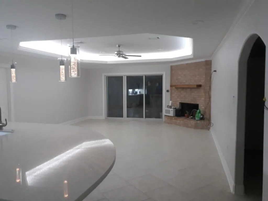 Open living room with a lit tray ceiling, tile floor, brick fireplace and sliding glass doors