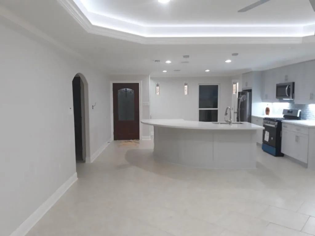 Open plan kitchen with a curved quartz island, white cabinets, tile floor and a lit tray ceiling