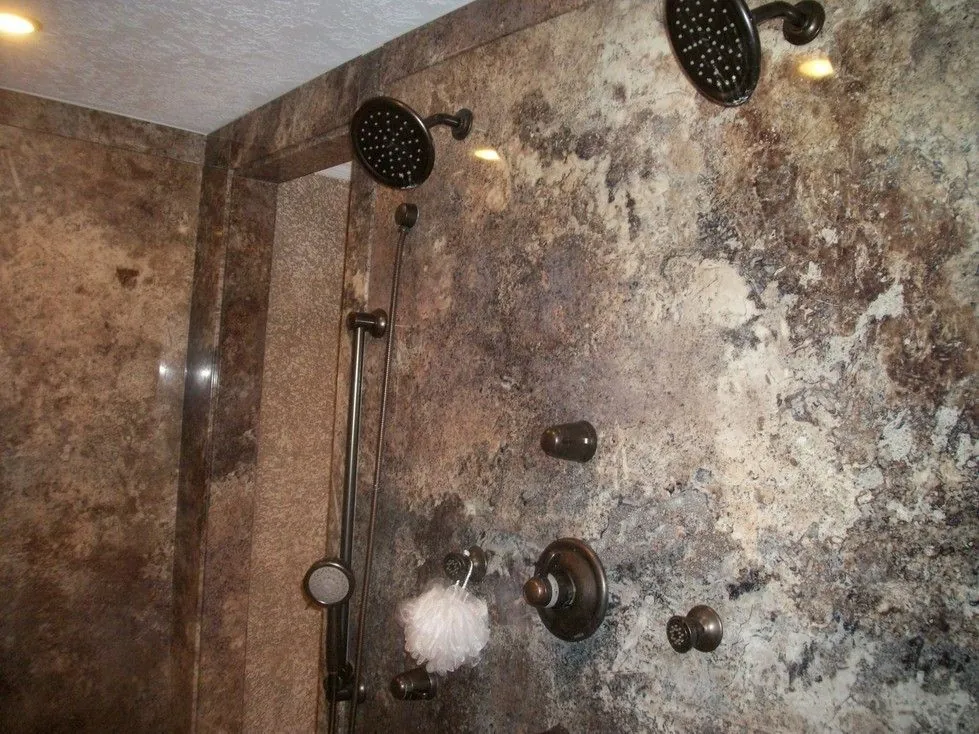Walk in shower with dark stone look wall panels, two rain shower heads and a handheld shower bar