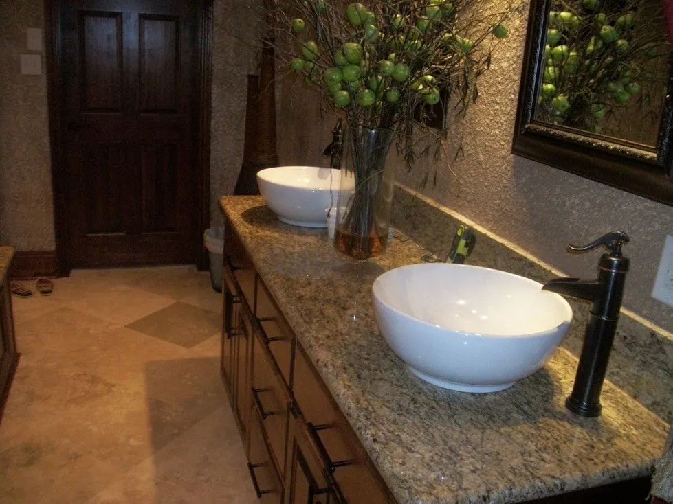 Double vessel sink vanity with a granite counter, wood cabinets and travertine style tile floor